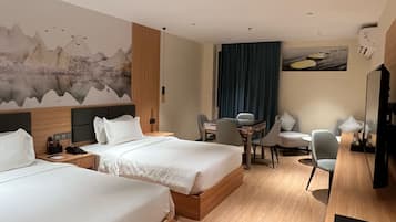 A hotel room with two beds, a desk, a chair, a dining table, and a TV.