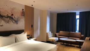 A hotel room with a bed, a sofa, a small table, a desk with a lamp, a painting on the wall, and a window with curtains. - Jinjiang Star Hotel (Pasay)