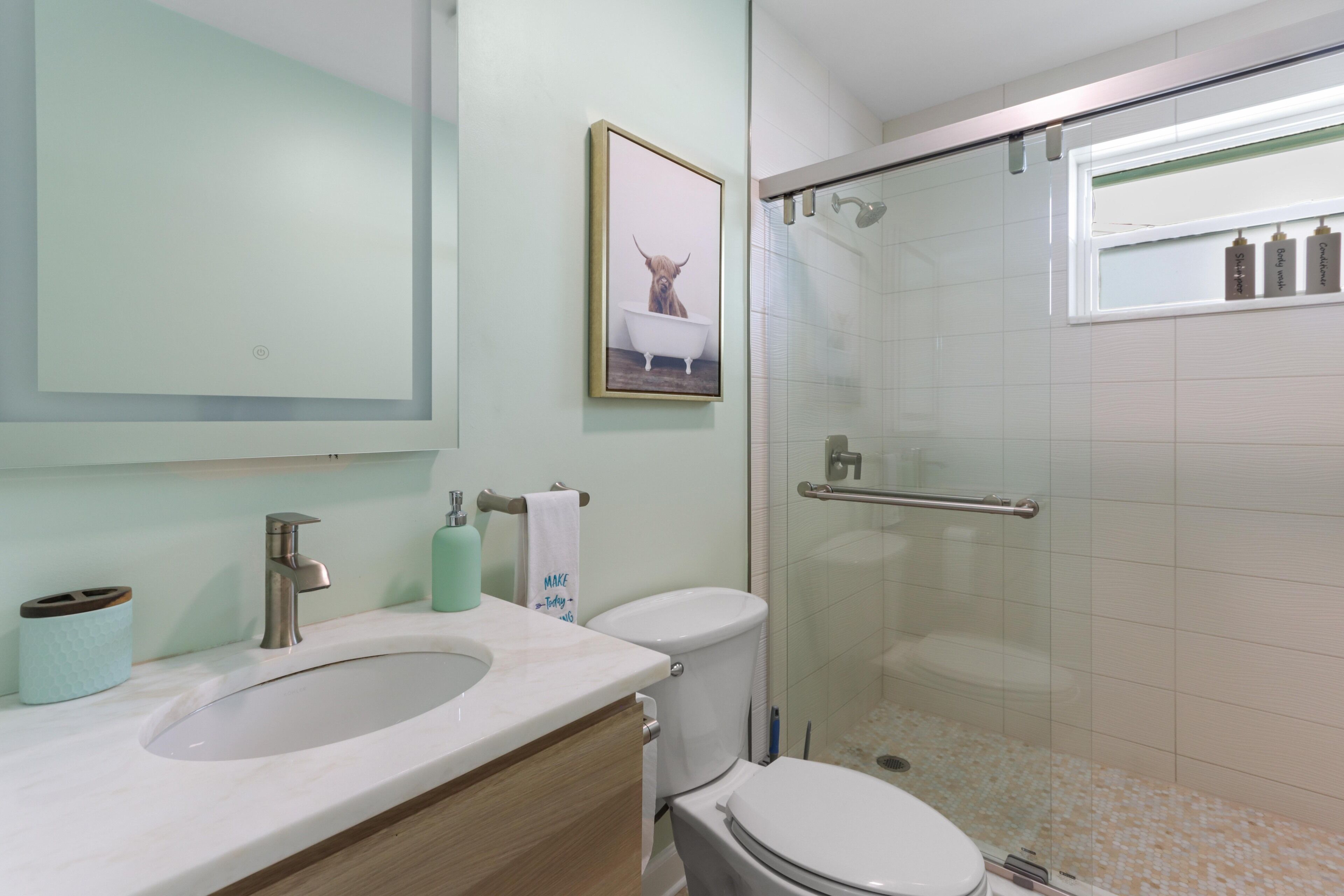 Baño con lavamanos, espejo, inodoro y cabina de ducha de vidrio.