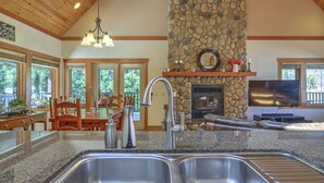 A kitchen with granite countertops, a stone fireplace, and a dining area with wooden furniture. - Blue Owl Villa - at Owl 's Head Mountain and minutes to the beach (SICAMOUS)
