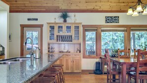 A kitchen with a granite countertop, wooden cabinets, and a dining area with wooden chairs and a table. - Blue Owl Villa - at Owl 's Head Mountain and minutes to the beach (SICAMOUS)