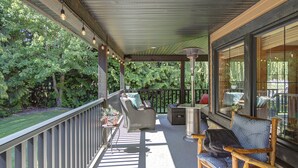 A covered outdoor patio with wicker furniture, a grill, and a view of a lush garden. - Blue Owl Villa - at Owl 's Head Mountain and minutes to the beach (SICAMOUS)