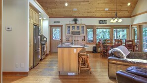 A spacious kitchen with wooden cabinets and a central island, a dining area with a wooden table and chairs, and a cozy seating area with a leather couch. - Blue Owl Villa - at Owl 's Head Mountain and minutes to the beach (SICAMOUS)