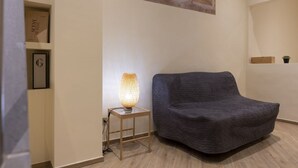 A cozy room with a dark grey sofa, a small wooden side table with a lamp, and a framed picture on the wall. - Chianti's Inn Sangiovese (Firenze)