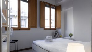 A bedroom with a bed, a desk, a chair, a lamp, and a window with wooden shutters. - Chianti's Inn Malvasia (Firenze)