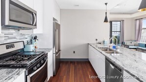 A modern kitchen with white cabinetry, a stainless steel range, a microwave, and a built-in oven. - Cityscape Apartment w/ Terrace - Leonard Luxury Apartment (Muskegon)