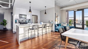 A modern kitchen with white cabinets, a central island with bar stools, and pendant lighting. - Cityscape Apartment w/ Terrace - Leonard Luxury Apartment (Muskegon)