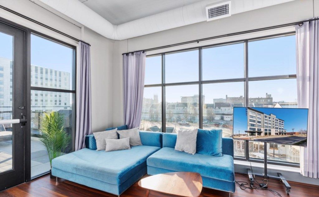 Una sala de estar moderna con un sofá seccional azul, ventanas amplias con vistas a la ciudad y una pequeña mesa de centro de madera.