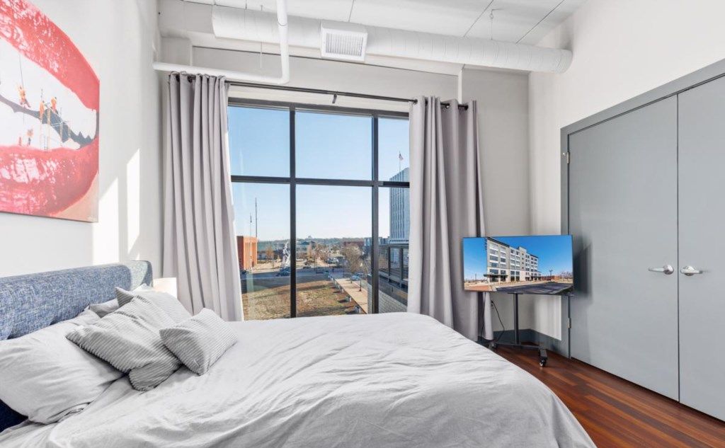 A bedroom with a large bed, a television on a stand, and a view of a cityscape through a large window.