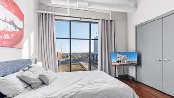 A bedroom with a large bed, a television on a stand, and a view of a cityscape through a large window.