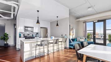 Une cuisine moderne avec des meubles blancs, un îlot central doté de tabourets et des luminaires suspendus.