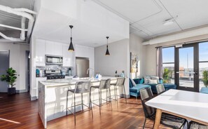 Uma cozinha moderna com armários brancos, uma ilha central com banquetas e iluminação pendente.