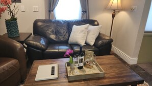 A living room with a leather sofa, a wooden coffee table with a tray of wine glasses, a remote control, and a book.