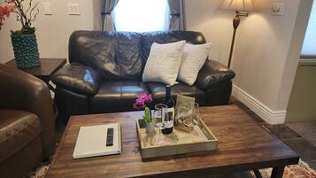 Una sala de estar con un sofá de cuero, una mesa de centro de madera con una bandeja de copas de vino, un control remoto y un libro.