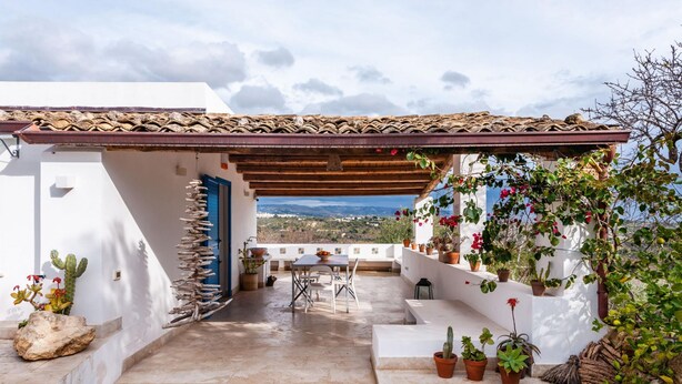 Un patio con una mesa y sillas, rodeado de plantas en macetas y vistas del paisaje.