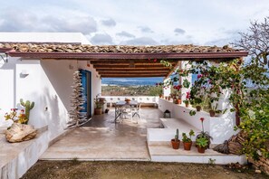 Un patio con una mesa y sillas, rodeado de plantas en macetas y vistas del paisaje.