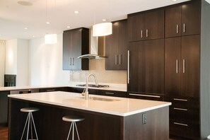 A modern kitchen with dark cabinetry, a central island with stools, and pendant lighting. - Luxury Townhome in Downtown Boulder - Club Access (Boulder)