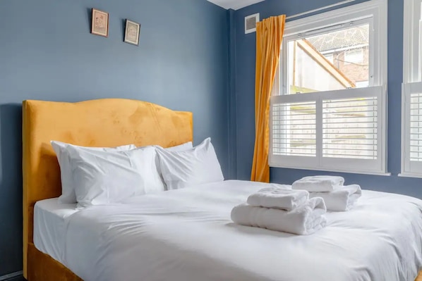 Cozy retreat with a single bed, white bedding, and a blue wall, featuring framed artwork and a window with white shutters.