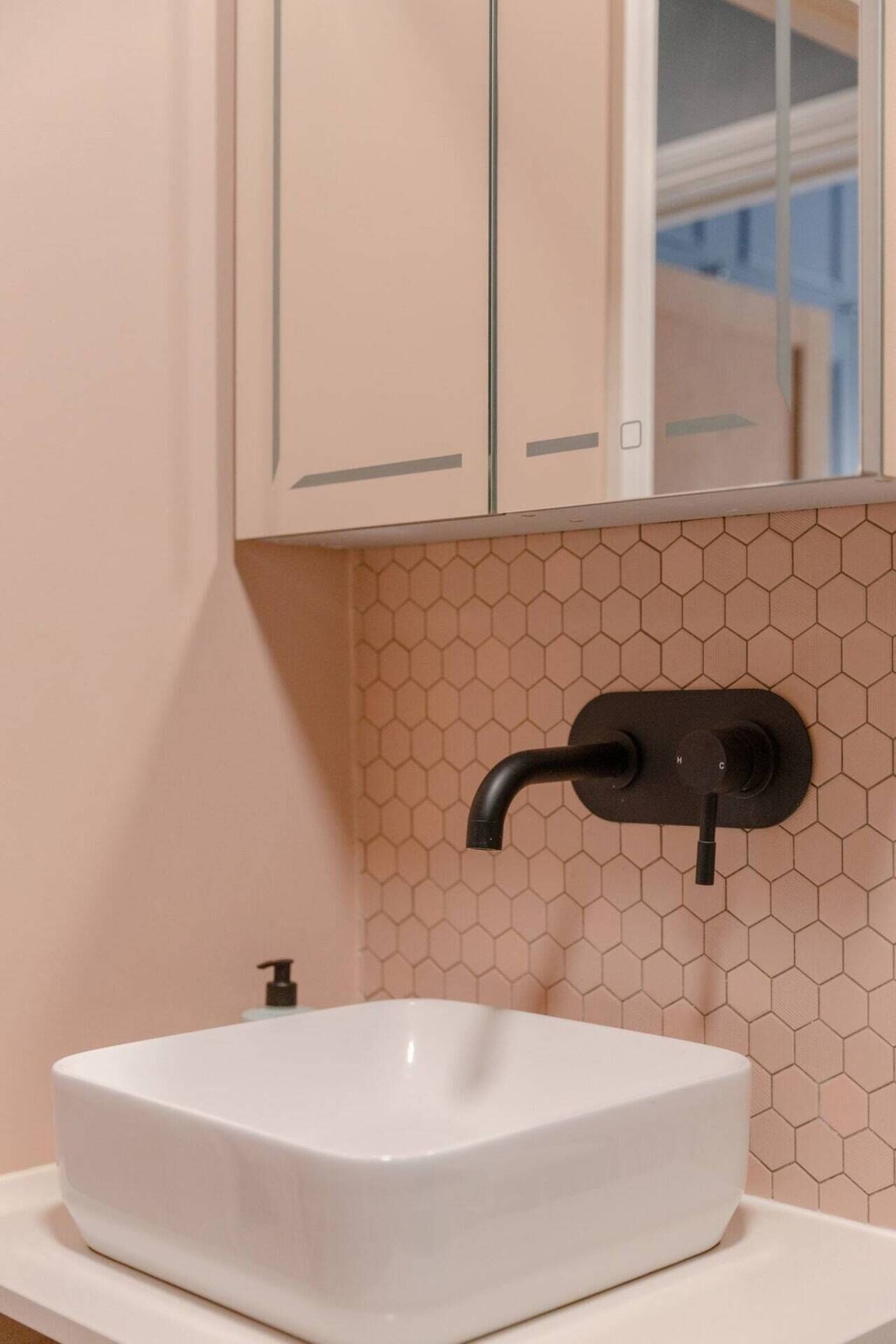 A bathroom with a white sink, a hexagonal patterned wall, and a mirror above the sink.