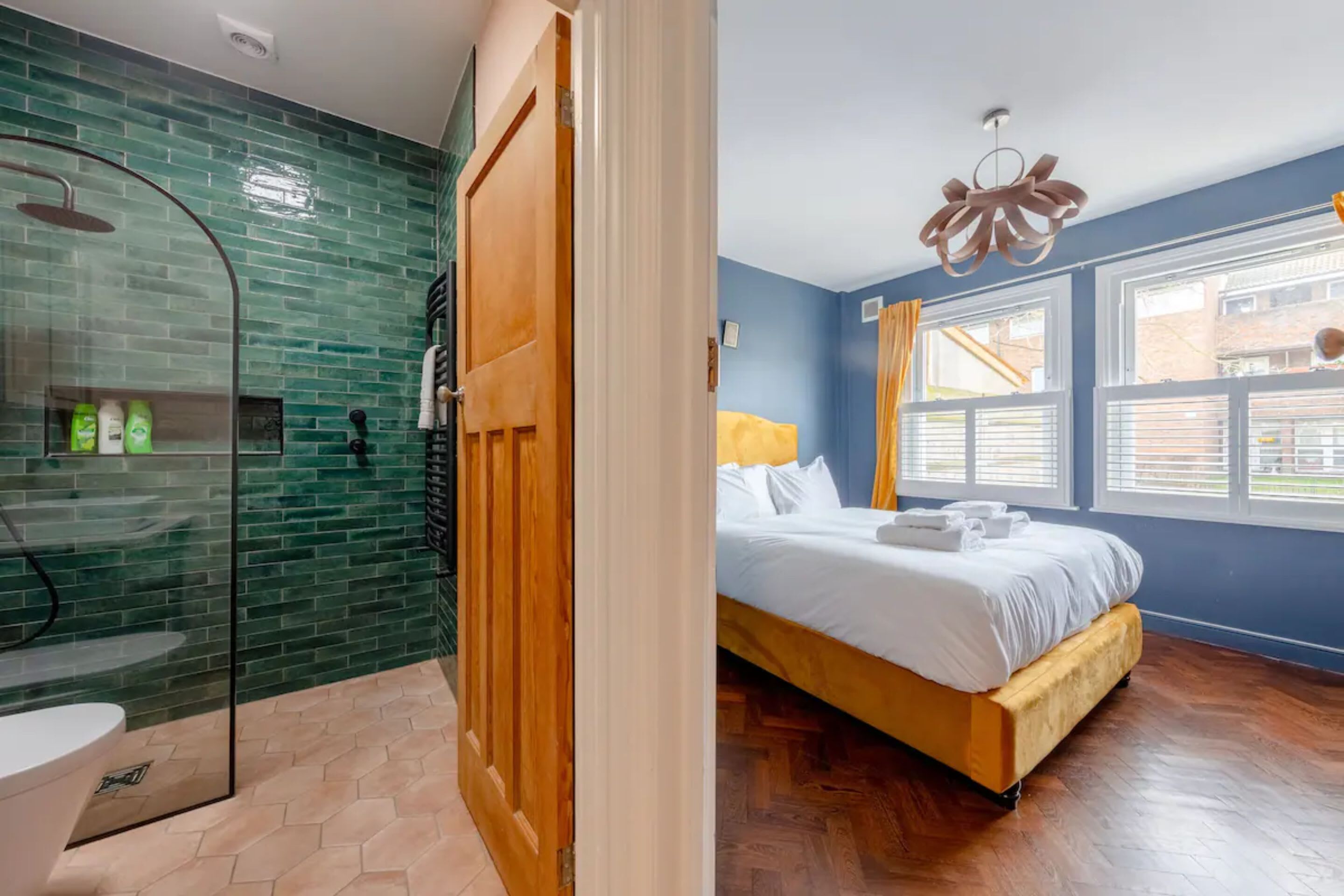 A room with a glass-enclosed shower, a wooden door, a bed with white linens, and a view of the outside through large windows.