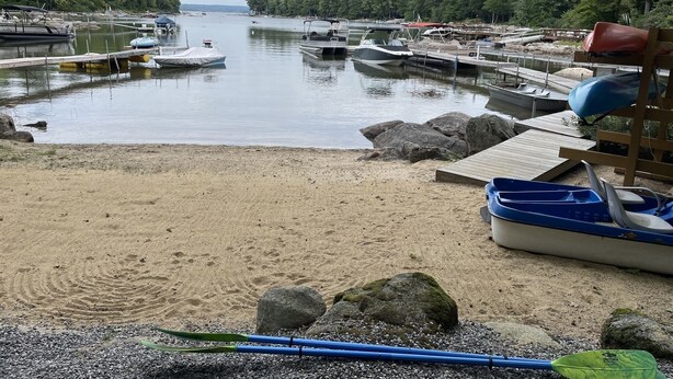 A marina with boats docked, a sandy beach, and a forested area in the background. - Blueberry More Limit 17 7 Bedroom Home by RedAwning (Raymond)