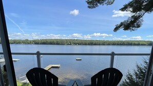 A balcony with two chairs facing a lake, a dock, and a forested shoreline. - Tremont Limit 10 4 Bedroom Villa by RedAwning (Bridgton)