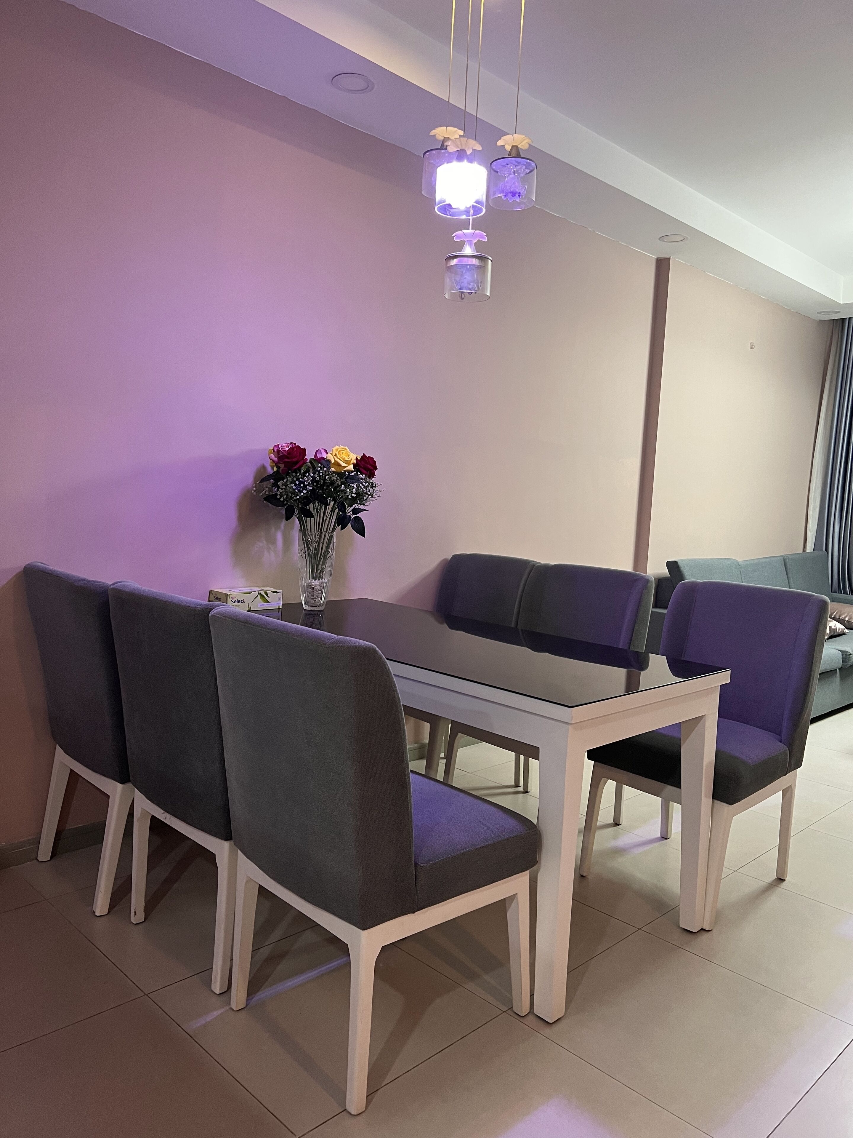 A dining area with a table and chairs, a vase with flowers, and a ceiling light fixture.