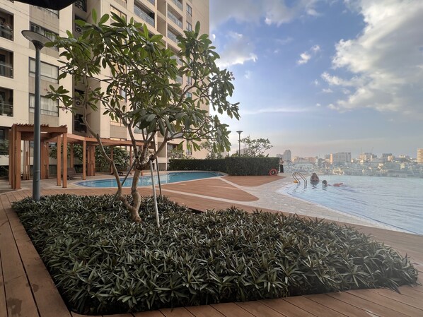 Une piscine sur le toit, offrant une vue sur les gratte-ciel de la ville, entourée de verdure et dotée d’une terrasse en bois.