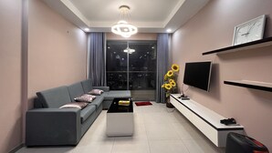 A modern living room with a grey sofa, a coffee table, a TV, and a wall-mounted shelf. - Supertramp House - Gold View Apartment (Ho Chi Minh City)