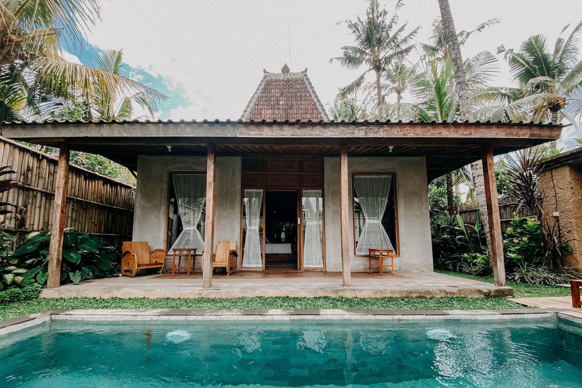 Une villa avec piscine, dotée d’un patio couvert, de deux chaises en bois et offrant une vue sur la piscine.