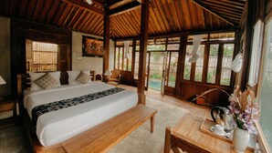 A wooden-framed bedroom with a bed, bedside tables, a bench, and a table with a vase of flowers. - Sarini Villas (Sukawati)