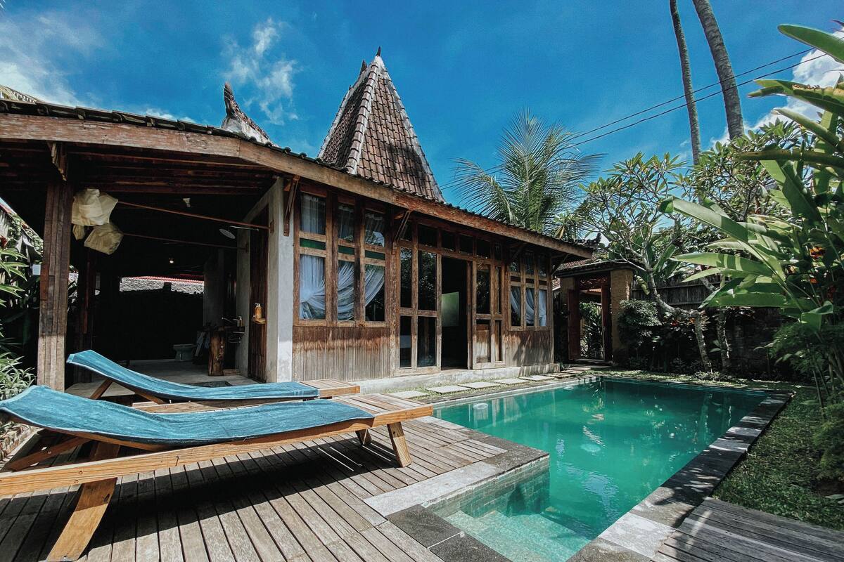 Une maison en bois avec un toit en tuiles, une piscine et des chaises longues.