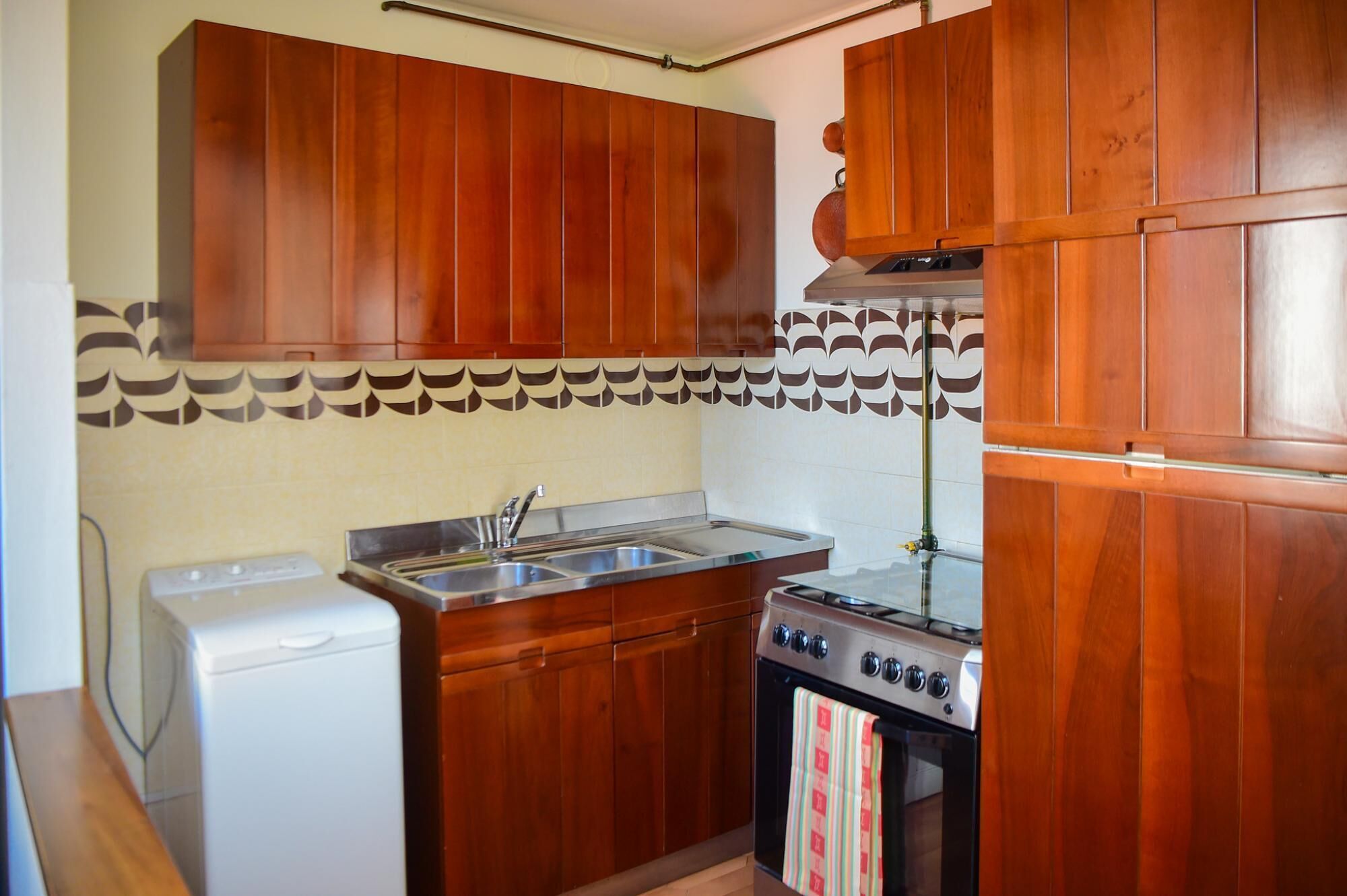 A kitchen with wooden cabinets, a stainless steel sink, a white washing machine, and a stove.