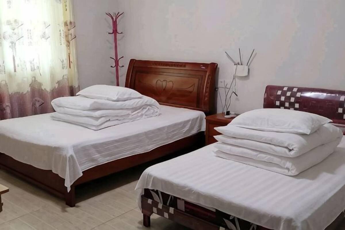 Two beds with white linens, a wooden headboard, a nightstand, and a wall-mounted lamp.