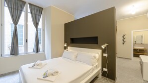Ein Hotelzimmer mit einem großen Bett, einem Nachttisch, einem an der Wand montierten Fernseher und einem Badezimmer mit Waschbecken und Spiegel.