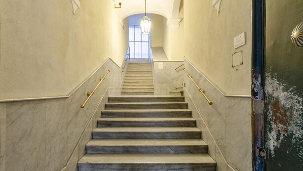 Eine Marmortreppe mit Handläufen, die zu einem hellen Raum mit einem Chandelier führt.