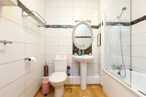 A bathroom with a toilet, sink, mirror, and glass-enclosed shower.