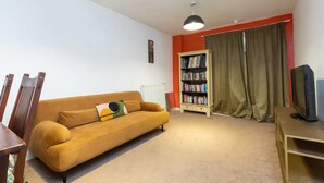 A living room with a sofa, a bookshelf, a television, and a radiator. - Cosy 1 Bedroom Flat in Shadwell (London)