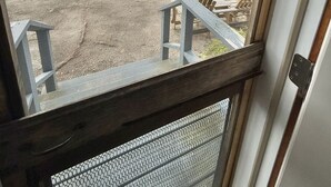 Blick aus einem Fenster auf einen Deckbereich mit Gartenmöbeln und eine natürliche Landschaft.