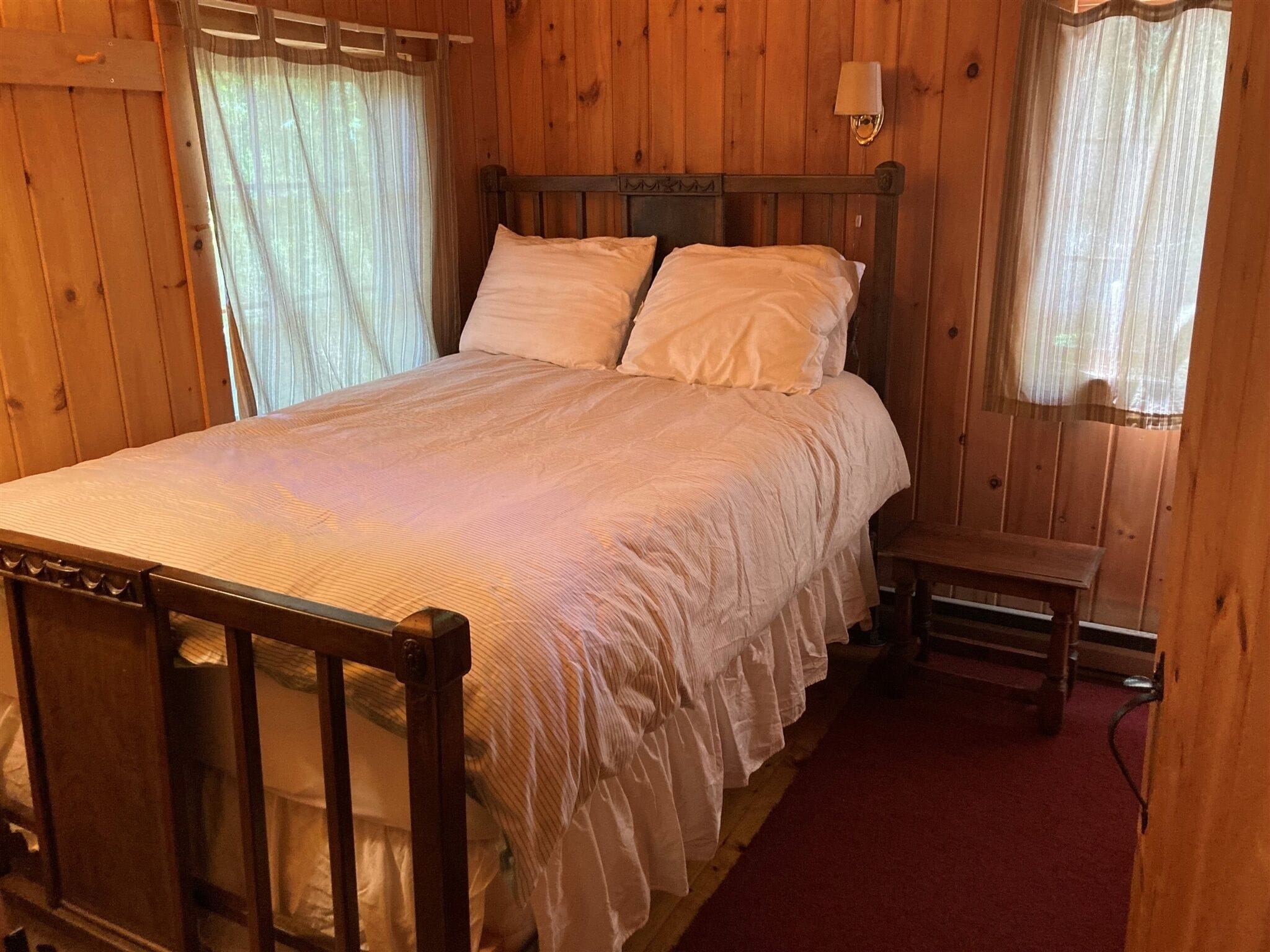 A wooden room with a bed, a nightstand, and a window with curtains.