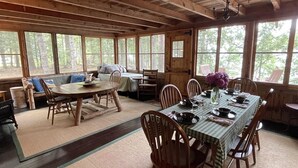 A rustic wooden cabin with a dining area featuring a table set for four, surrounded by wooden chairs. - Mackinney Camp - Limit 8 4 Bedroom Cottage by RedAwning (Standish)