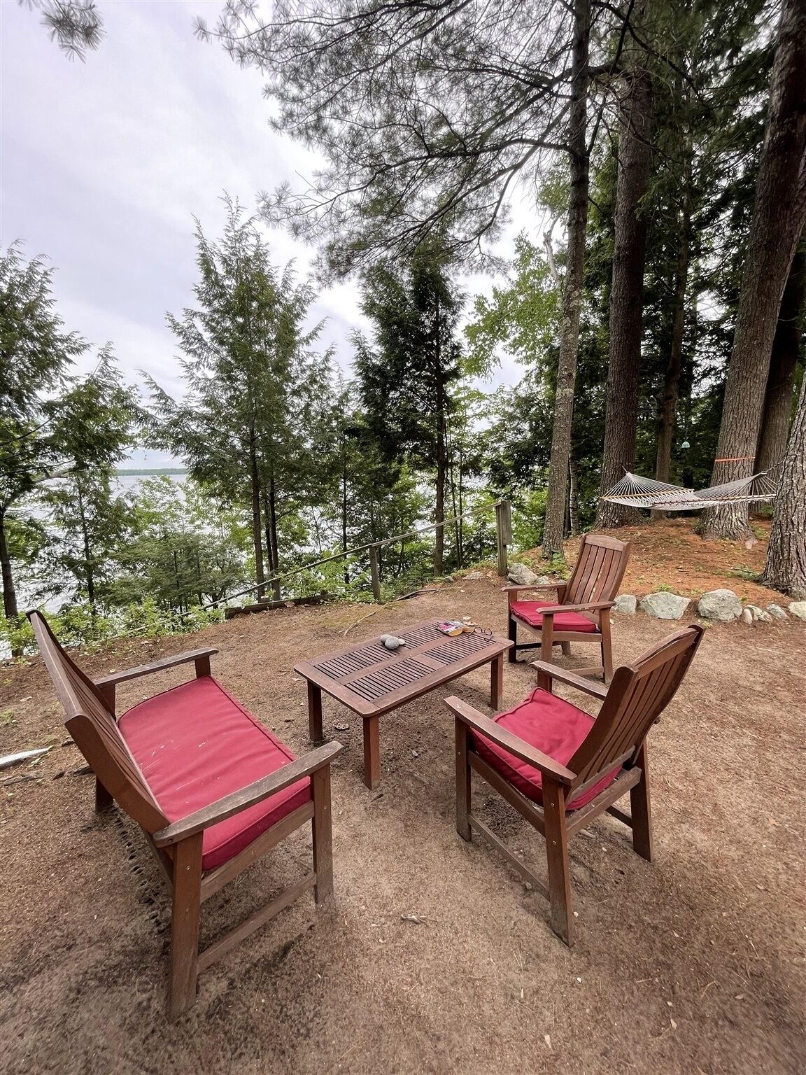 Een buitenruimte met houten stoelen en een tafel, omringd door bomen en uitzicht op het water.