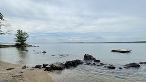 A rocky shoreline with clear water, a small boat, and a distant tree. - Mackinney Camp - Limit 8 4 Bedroom Cottage by RedAwning (Standish)