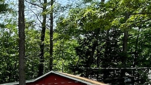 Une maison rouge à un étage, dotée d’un porche à l’avant et entourée d’arbres.