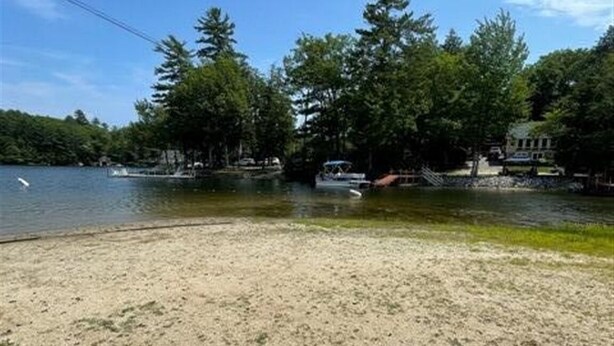 Une plage de sable bordée d’un lac, d’arbres et d’un quai où sont amarrés des bateaux.