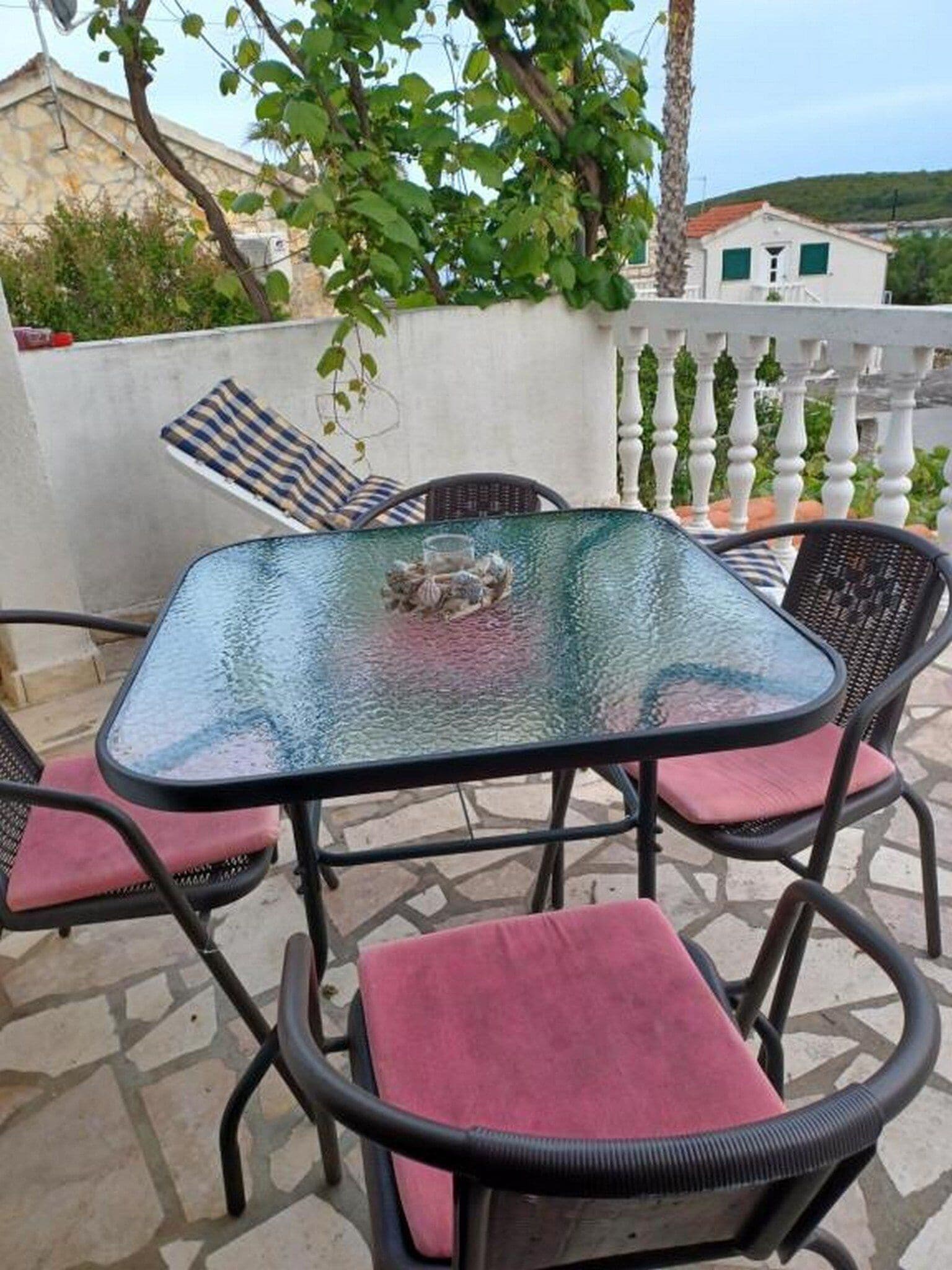 Um pátio externo com uma mesa de vidro e quatro cadeiras, cada uma com uma almofada.