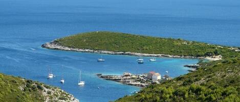 Paisaje costero con una pequeña isla, barcos y algunos edificios.