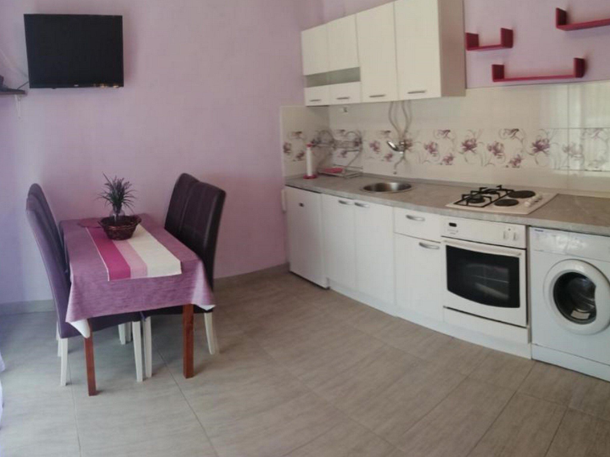 A compact kitchen with white cabinets, a built-in oven, a washing machine, and a dining area with a table and chairs.