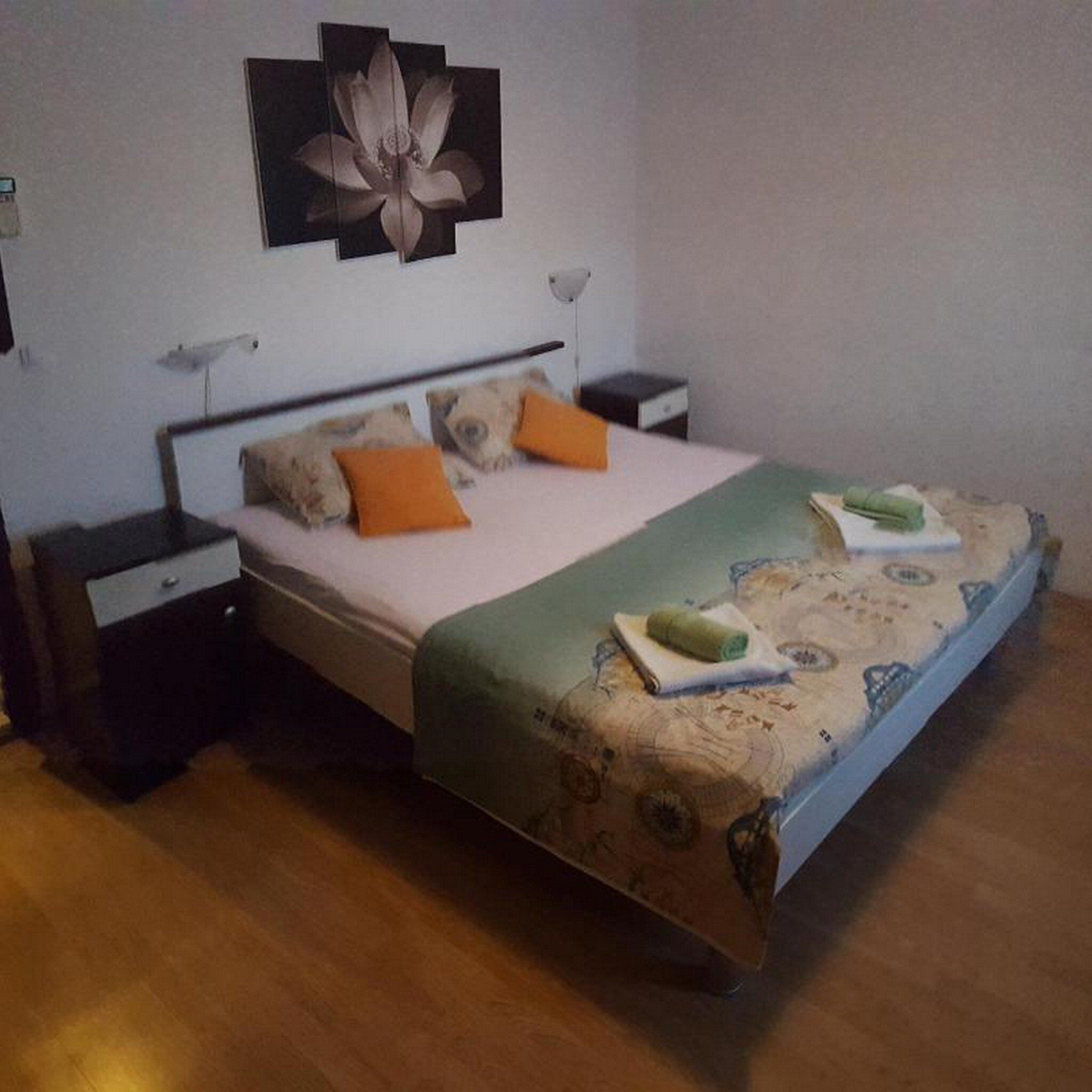 A bedroom with a bed, two nightstands, a wall-mounted lamp, and a flower painting.