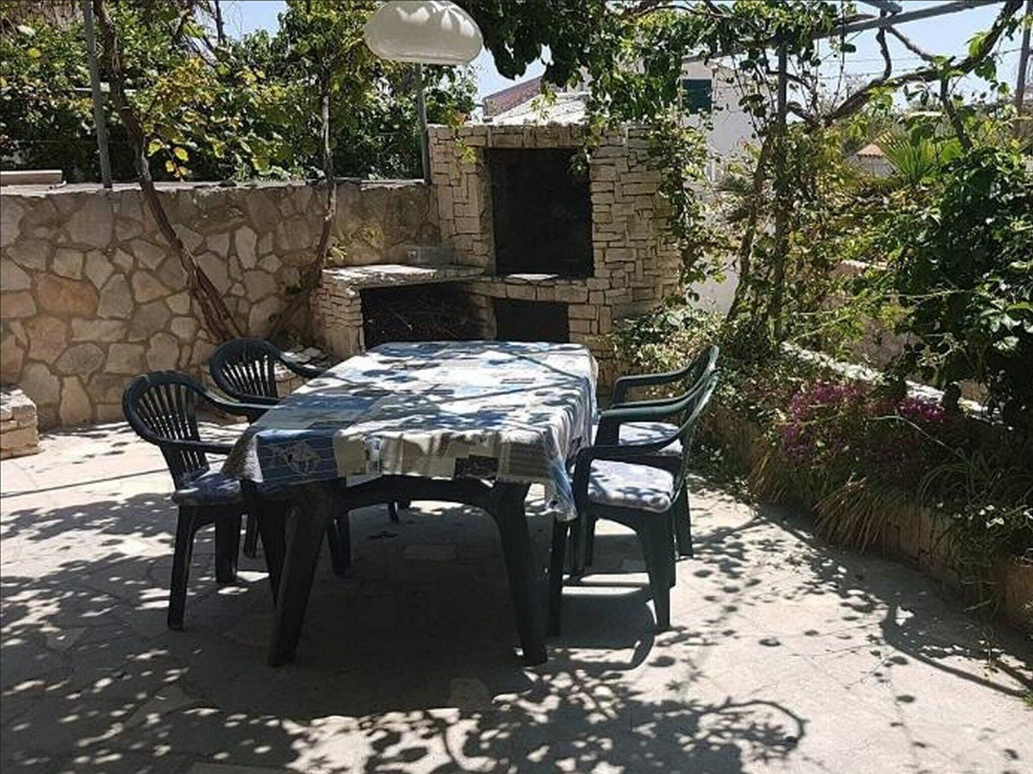 An outdoor patio with a stone wall, a table with a tablecloth, and chairs.